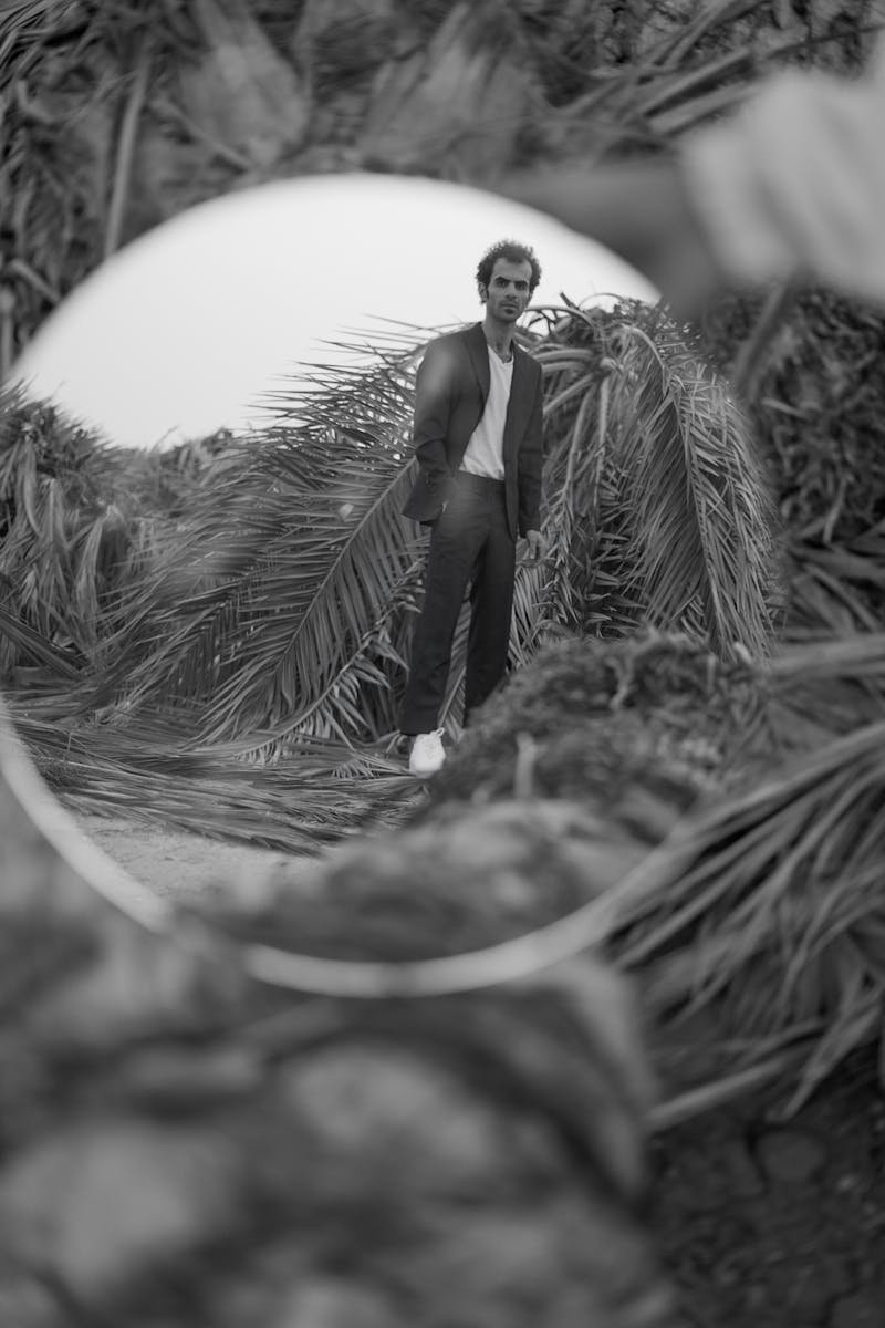 Monochrome image capturing a creative reflection of a man posing amid palm trees.